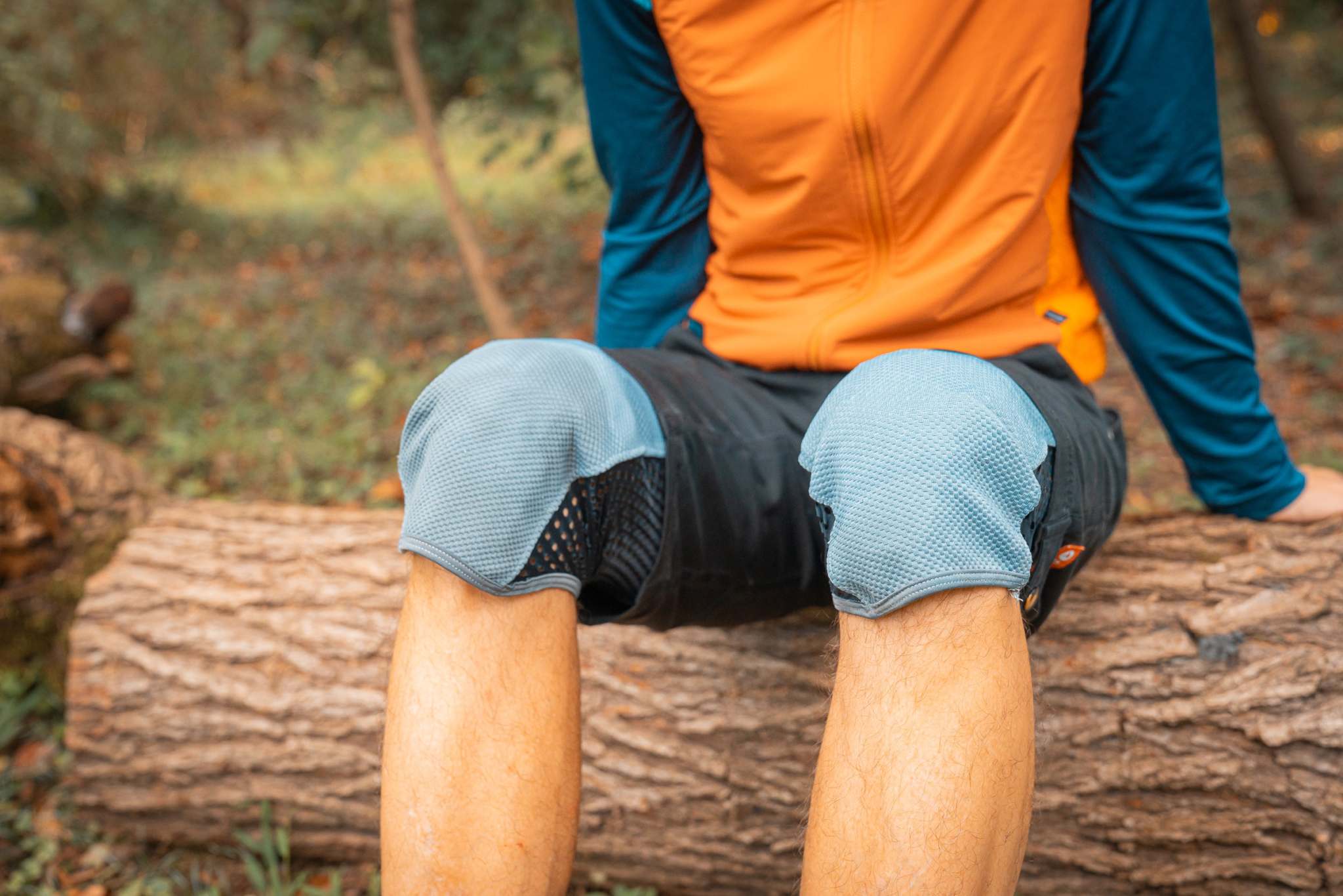 Mountain biker wearing Moxie Cycling All Gender Trail Pants with built-in knee pads sitting on a log outdoors.